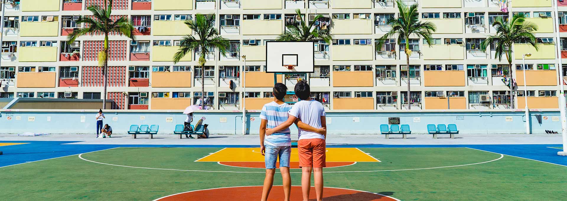 Two people standing on a basketball court with their arms around each other staring at a multistory building