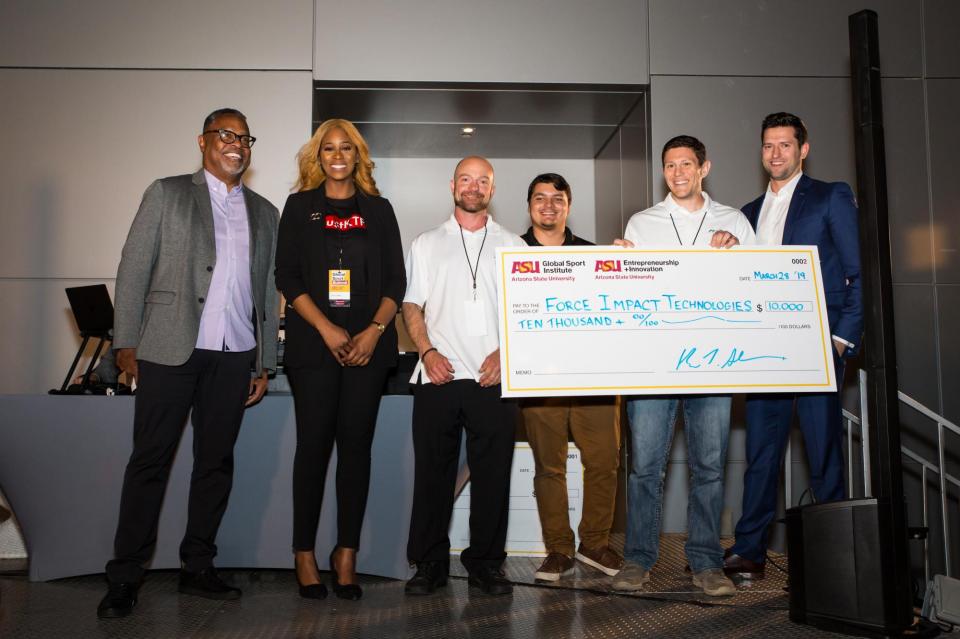 A group of sport entrepreneurs stand on stage, one holding an oversized check with their funding amount displayed.