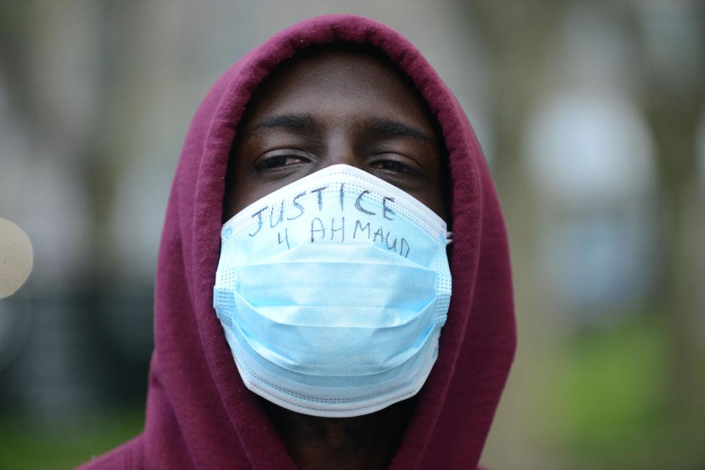 A protestort wears a maroon hoodie and a blue medical mask with the words handwritten over it "Justice 4 Ahmaud." (Photo by B.A. Van Sise/NurPhoto via Getty Images)
