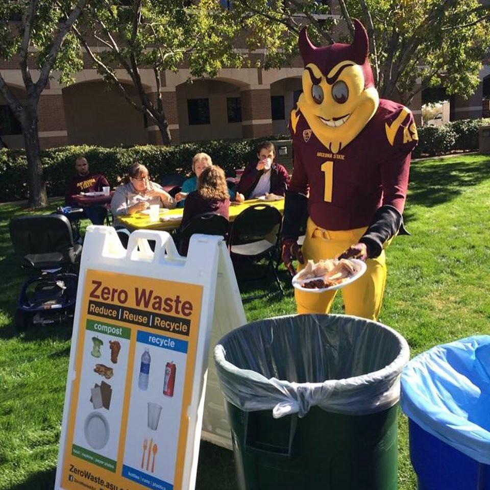 Sparky the ASU mascot stands in front of different waste bins with a plate.