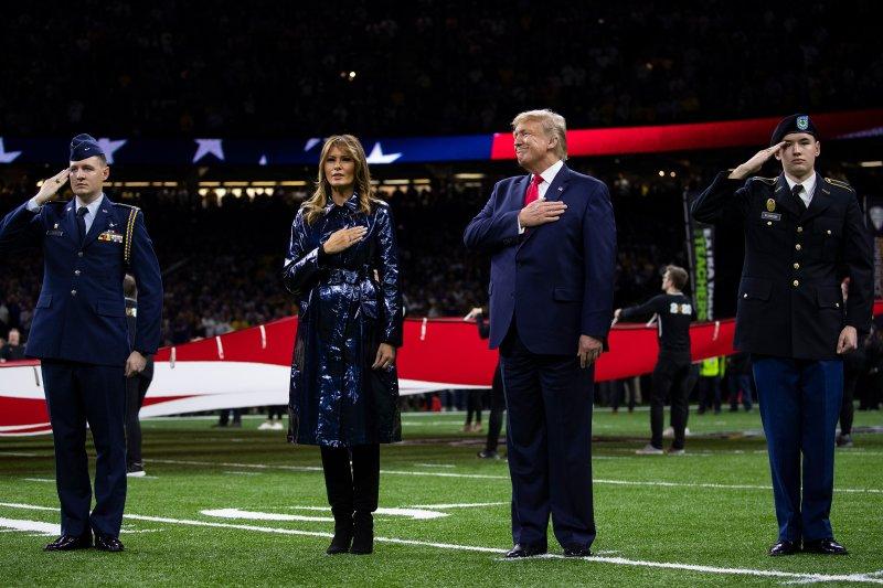 Trump and wife with hands across their chest and two soldiers saluting 